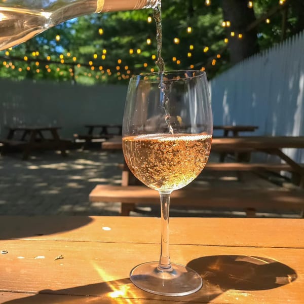 White wine pouring into a glass on a wooden table at The Pieman Pizza's outdoor patio.