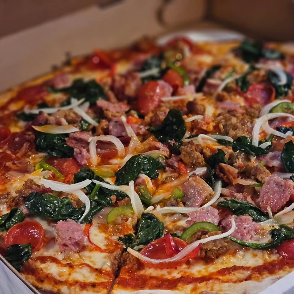 A close-up of a Pieman Pizza with various toppings, including sausage, spinach, and onions.