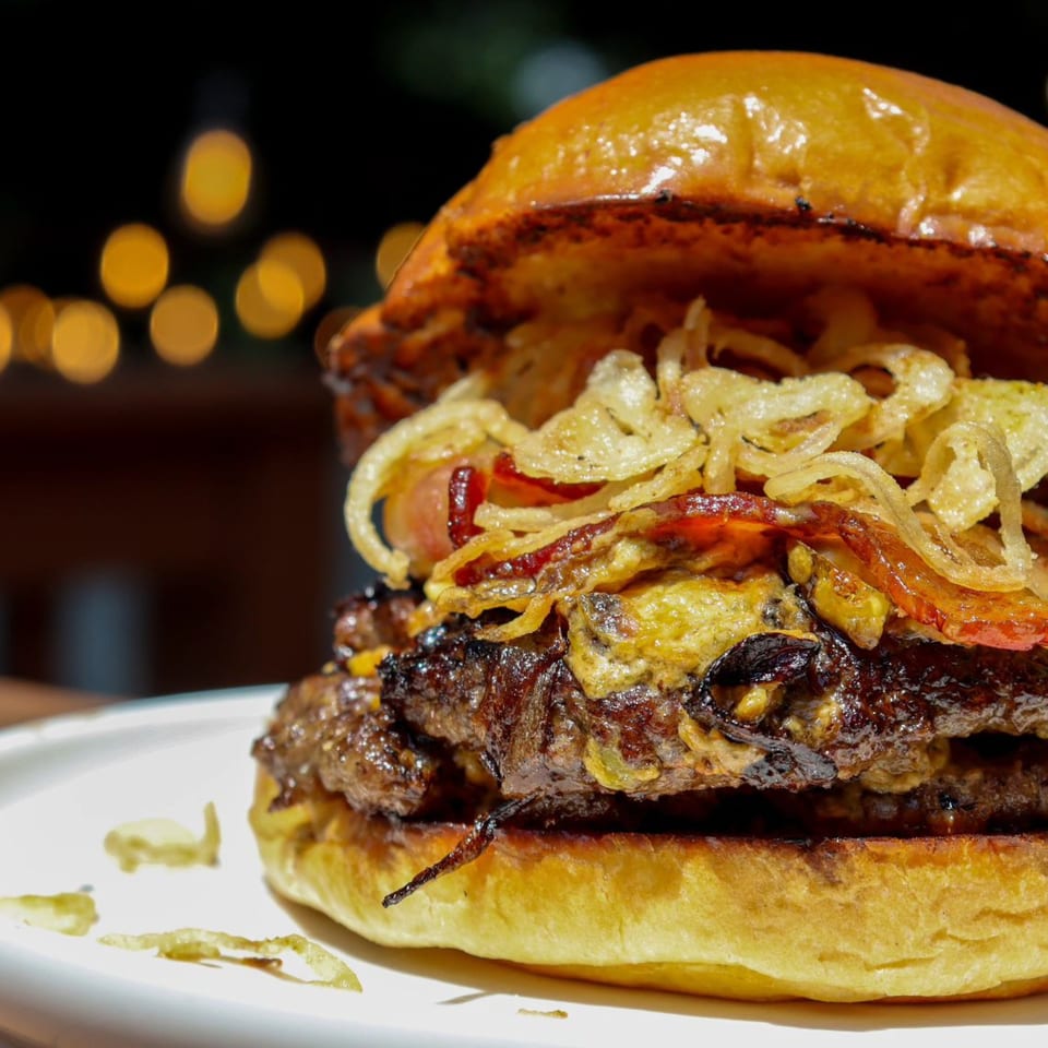 Close-up of a juicy burger with crispy fried onions and bacon on a brioche bun.