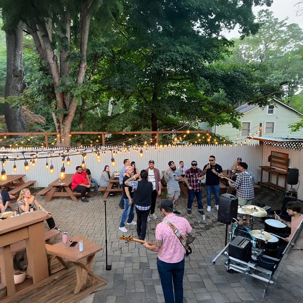 Outdoor patio at The Pieman Pizza with string lights, picnic tables, and a live band performing.