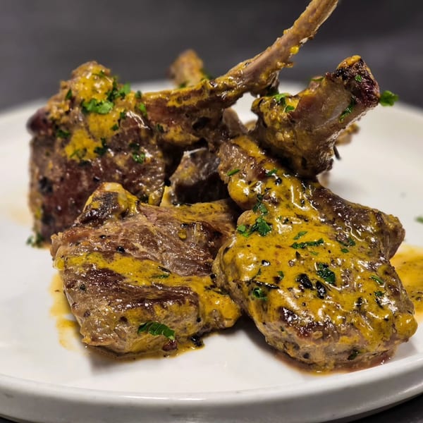 Lamb chops with a yellow sauce and green herbs on a white plate.