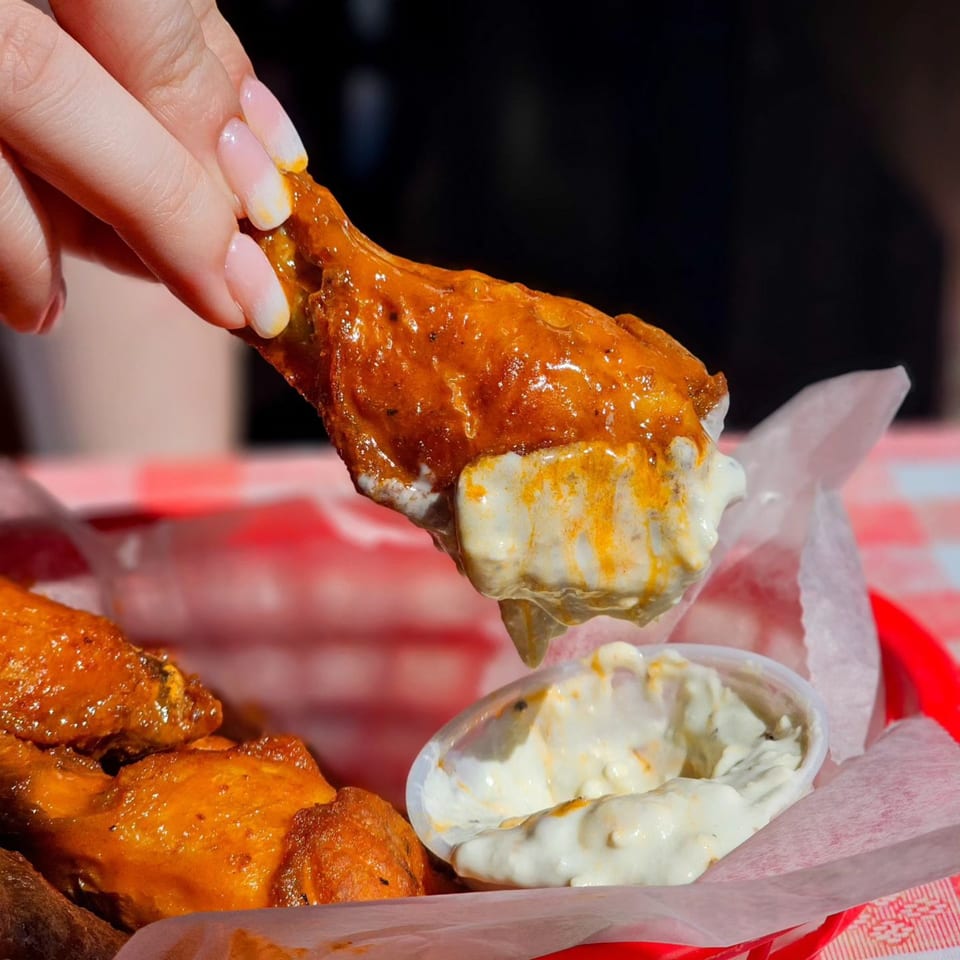 A hand dips a buffalo chicken wing into a small container of creamy white sauce.