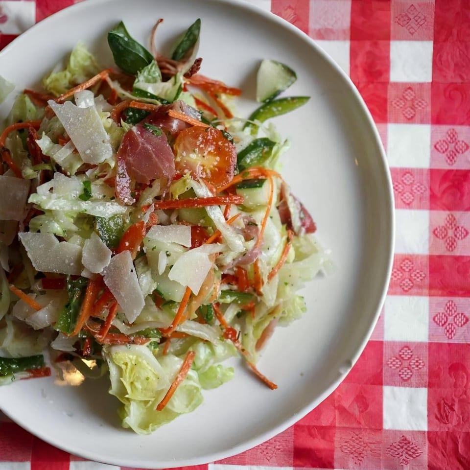 Fresh garden salad with shaved parmesan, tomatoes, and carrots on a white plate.