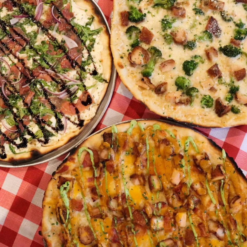 Three gourmet pizzas from The Pieman Pizza, including one with prosciutto, arugula, and balsamic glaze.