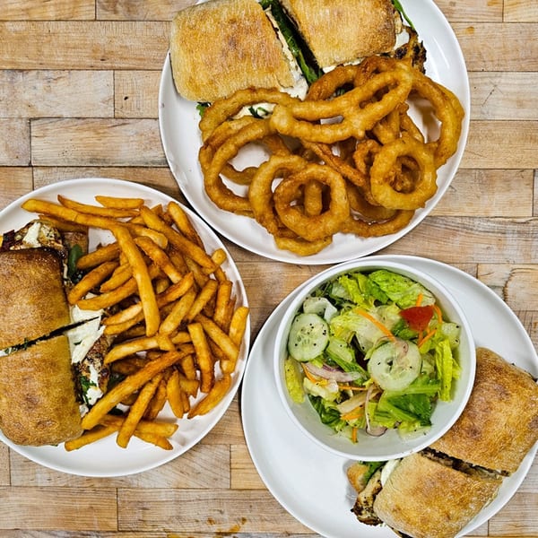 Three plates of sandwiches with sides of fries, onion rings, and a garden salad.