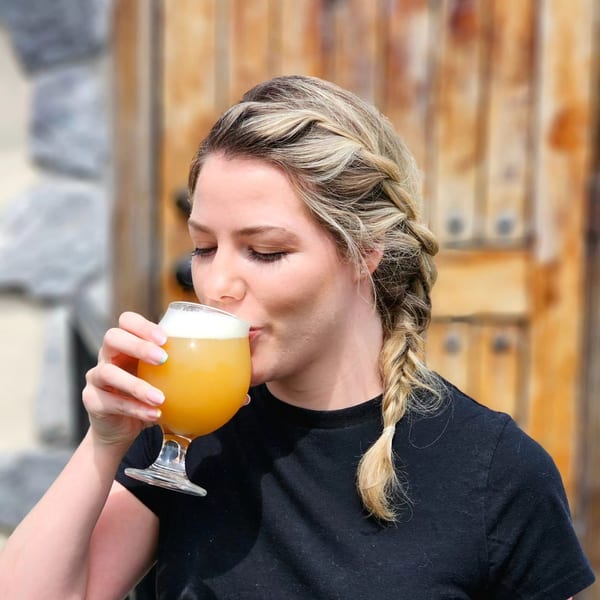 A woman with braided blonde hair sips a frothy orange drink from a stemmed glass.